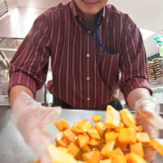 person stirs squash cubes with a gloved hand